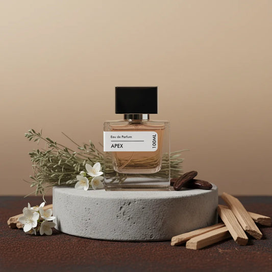 Apex Eau de Parfum 100ml bottle with black cap, surrounded by white flowers, green herbs, and wooden sticks on a concrete sta