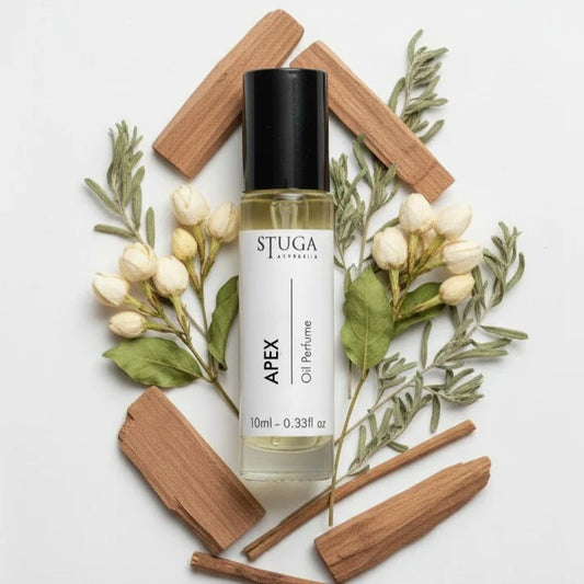10ml Stuga Apex oil perfume bottle surrounded by white flower buds, green leaves, and wooden sticks on white background