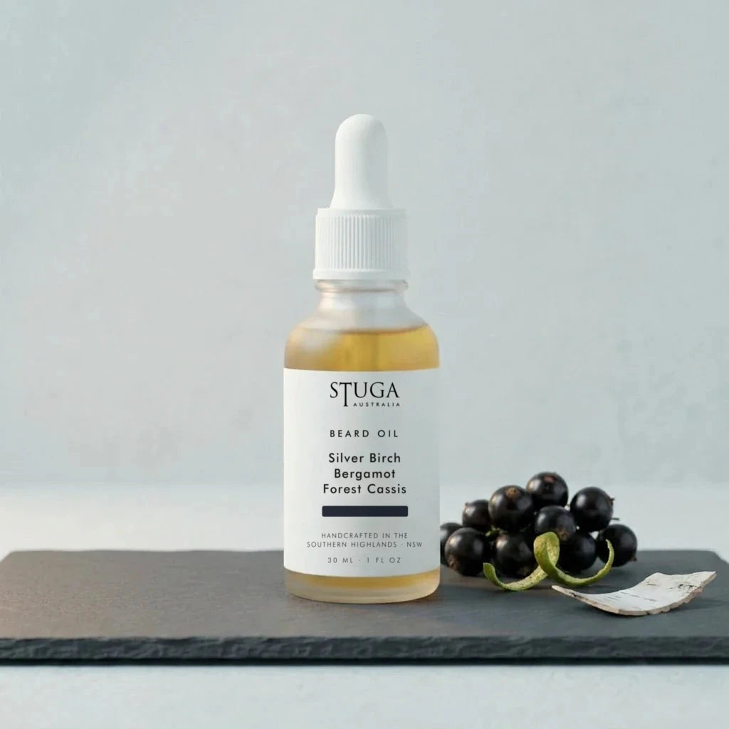 Stuga Beard Oil in Silver Birch, Bergamot and Forest Cassis — amber oil in a glass dropper bottle on a slate slab with fresh blackcurrants and curls of birch bark. Made fresh to order with Australian sweet almond, macadamia and apricot kernel oils, handcrafted in the Southern Highlands, NSW Australia.