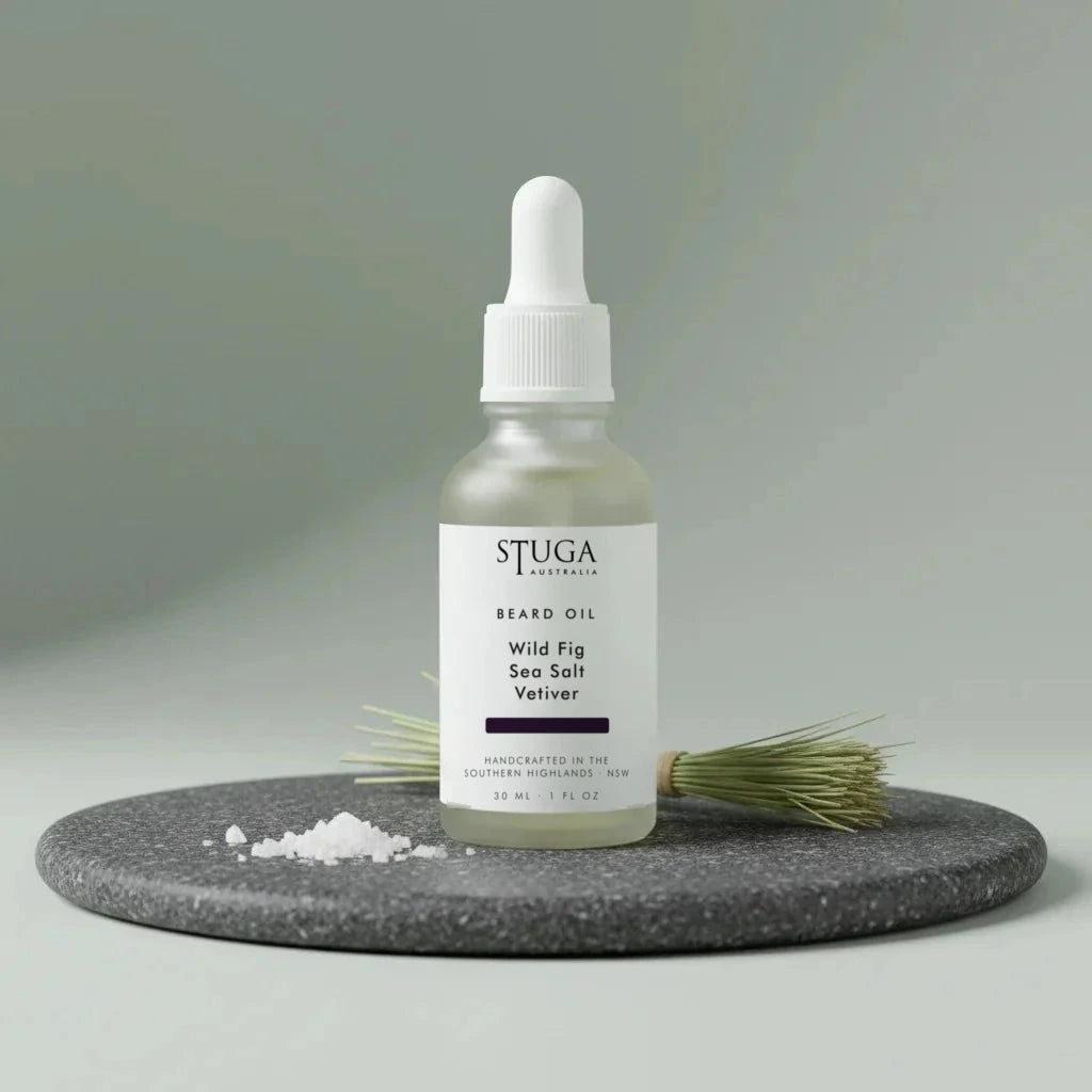 Stuga Beard Oil in Wild Fig, Sea Salt and Vetiver — pale oil in a frosted glass dropper bottle on a dark granite disc with flaked sea salt and a bundle of vetiver root. Made fresh to order with Australian sweet almond, macadamia and apricot kernel oils, handcrafted in the Southern Highlands, NSW Australia.