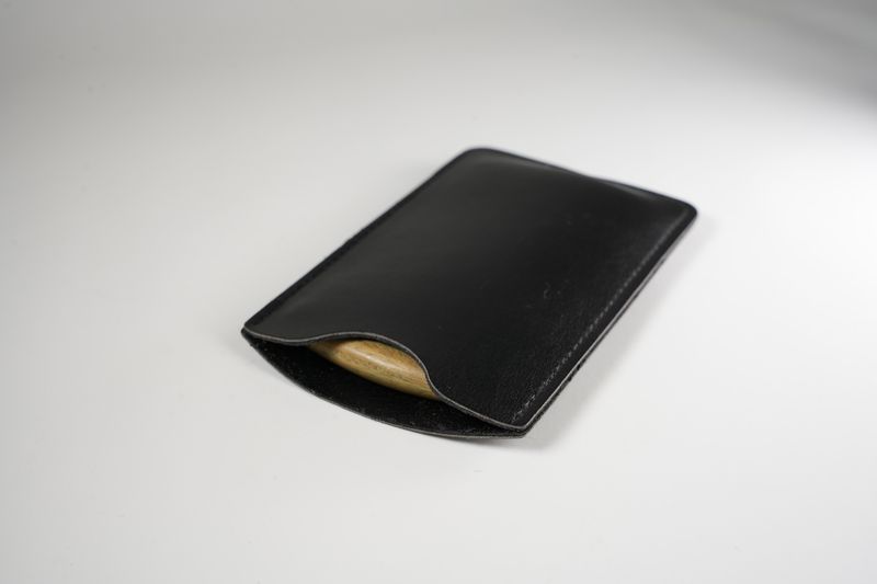 Black leather card holder sleeve with smooth finish holding a wooden object inside