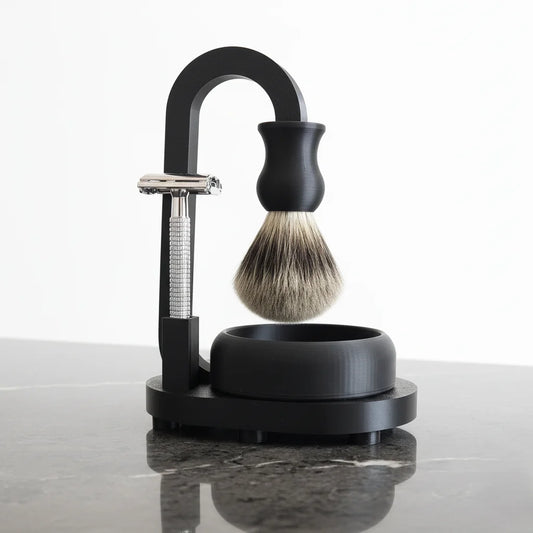 Black shaving stand with safety razor, badger hair brush, and bowl on a marble counter.