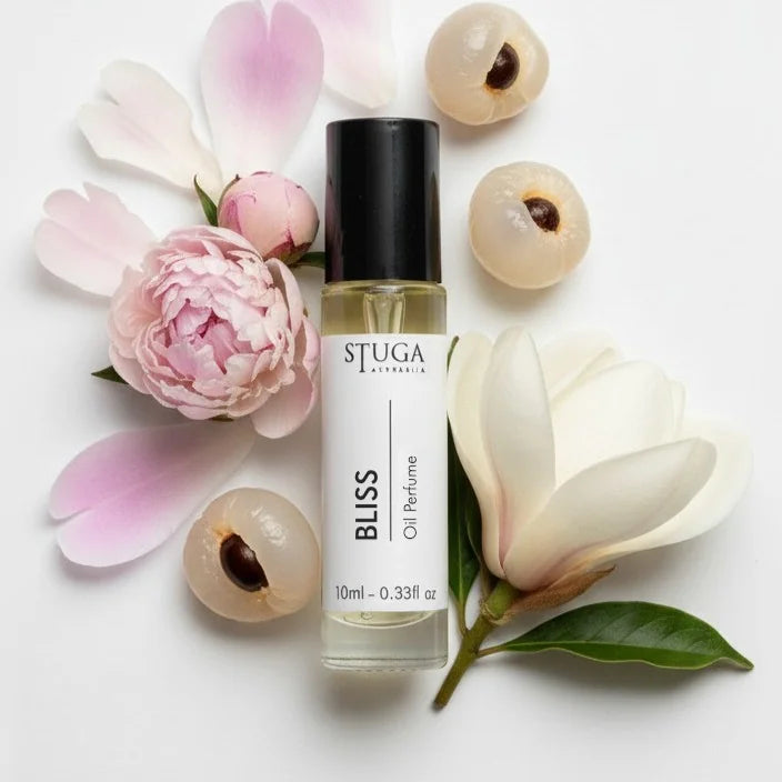 10ml Bliss oil perfume bottle surrounded by pink peony, white magnolia flowers, and lychee fruits on white background