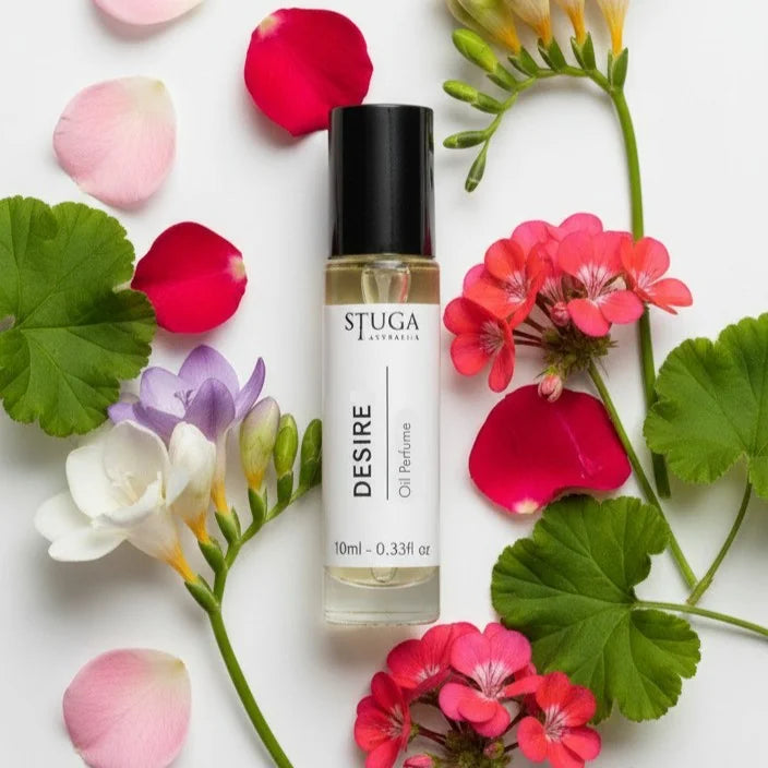 10ml Desire oil perfume by Stuga Australia surrounded by pink, red, purple, and white flowers and green leaves