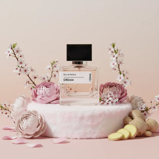 Dream Eau de Parfum 100ml bottle with black cap, surrounded by pink peonies, white cherry blossoms, and ginger slices on a pi