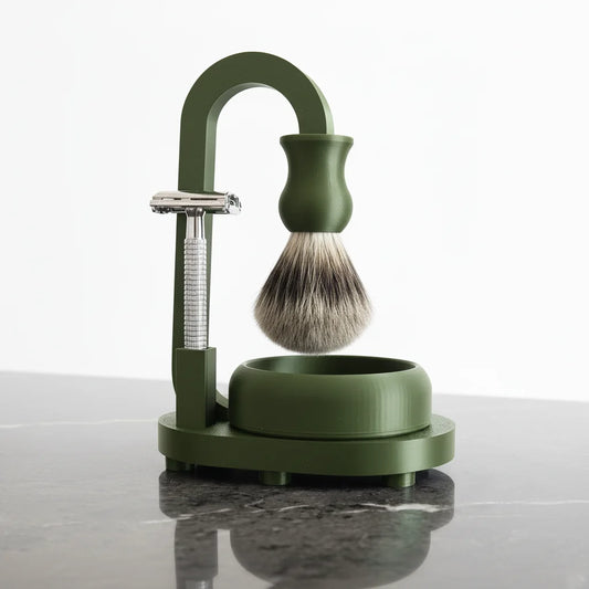 Dark green shaving stand with silver safety razor, badger hair brush, and bowl for men's grooming.
