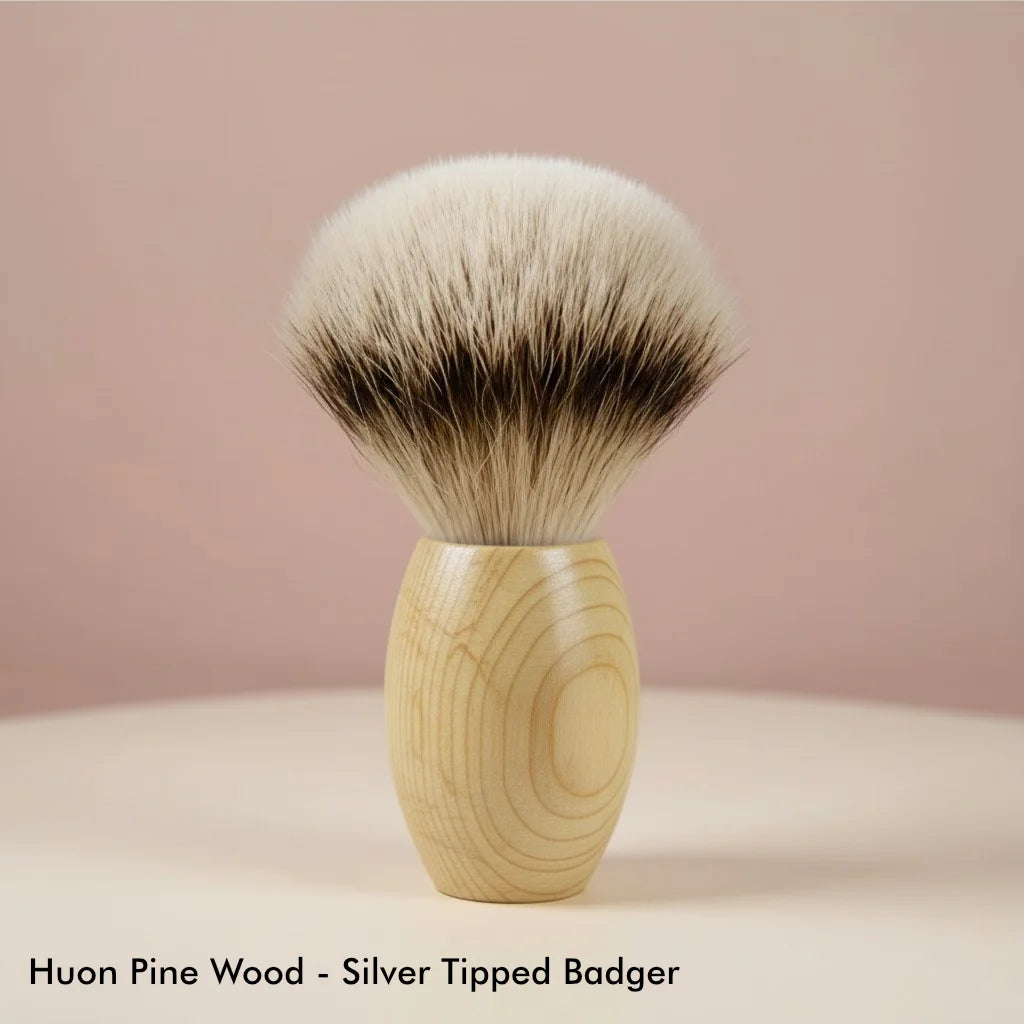 Shaving brush with light huon pine wood handle and silver tipped badger bristles, standing upright.