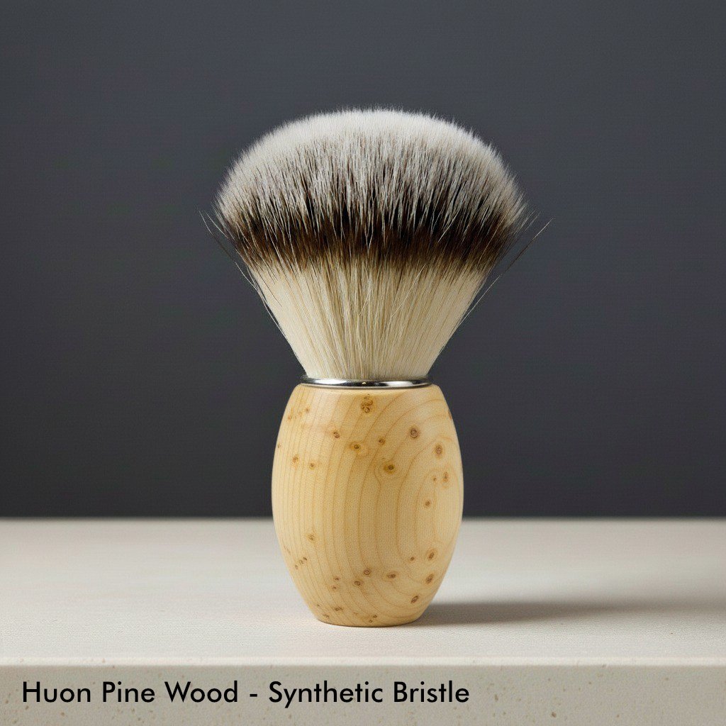 Huon pine wood shaving brush with light brown and white synthetic bristles, silver collar, on a light surface.