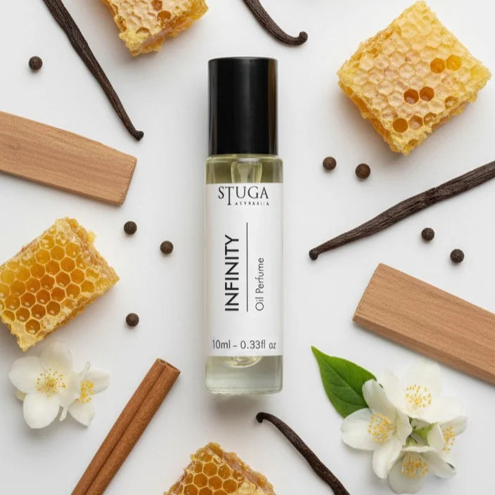 10ml bottle of Stuga Infinity oil perfume surrounded by honeycomb, vanilla pods, cinnamon sticks, jasmine flowers, and wooden