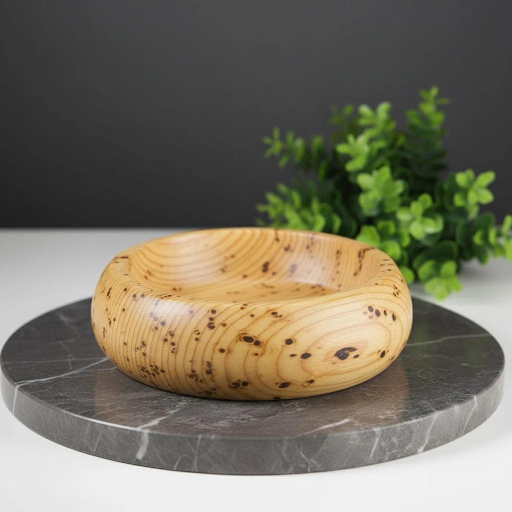 Hand-turned knotty Huon pine wood shaving bowl with natural grain and dark flecks, smooth finish, on a marble surface.