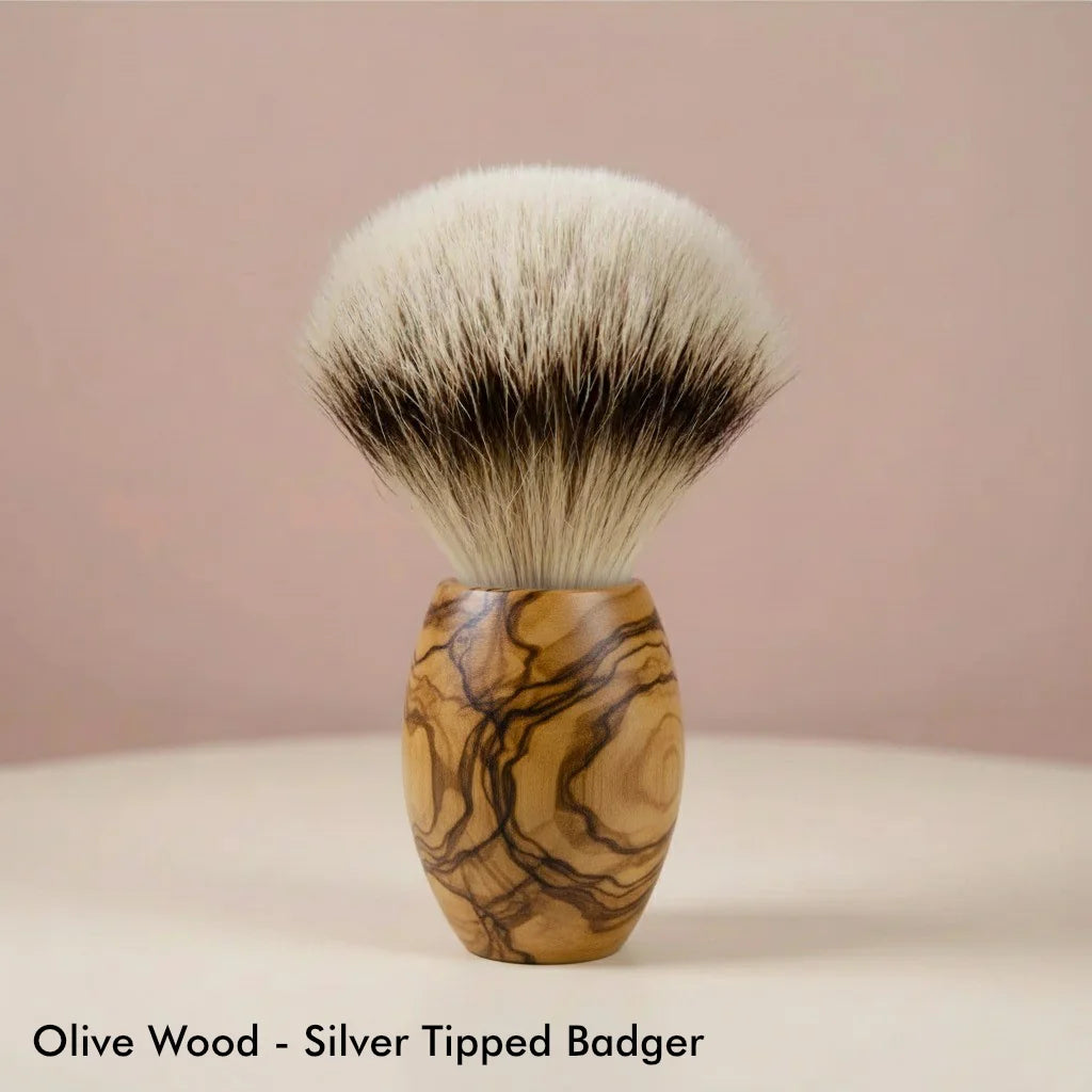 Close-up of a shaving brush with a natural olive wood handle and soft, silver-tipped badger bristles, standing upright.