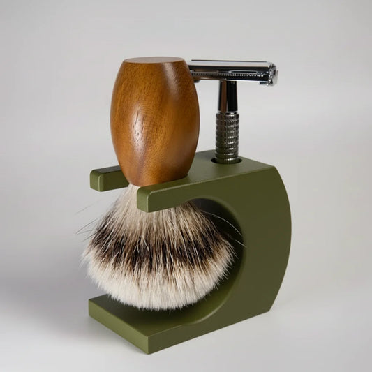 Shaving brush with wooden handle and metal razor on a green stand against a white background