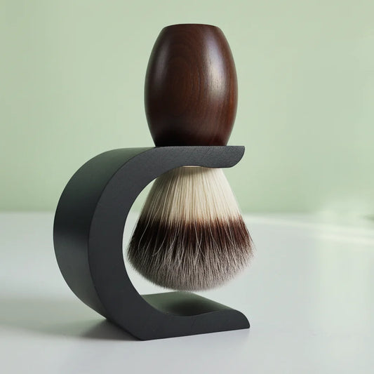 Dark wood shaving brush with badger hair bristles on a black curved stand, against a light green background.