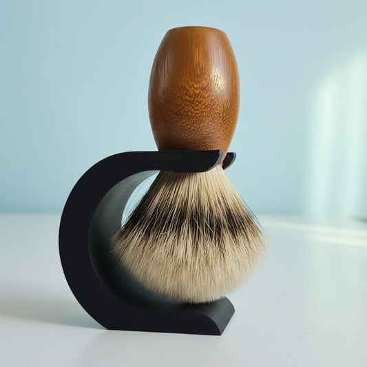 Classic shaving brush with light wood handle and badger hair bristles, resting in a sleek black stand.