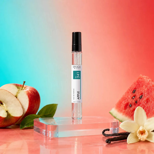 Stuga Apple No. 341 apple perfume, 10ml eau de parfum spray bottle with a black cap on a clear acrylic block, with a halved red apple, a slice of watermelon, vanilla pods and a vanilla flower.