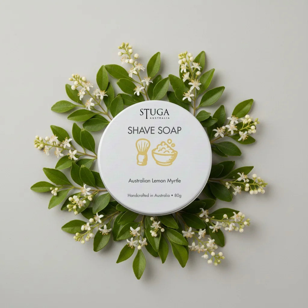 Stuga Australia Australian Lemon Myrtle Shave Soap in a white tin, surrounded by green leaves and small white flowers.