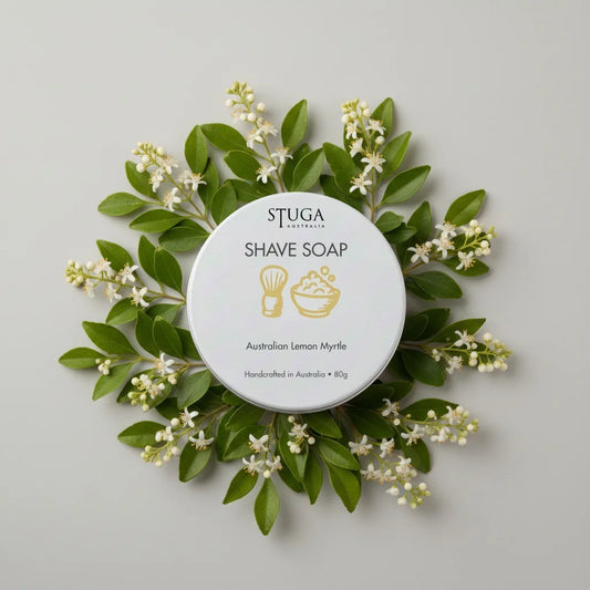 Stuga Australia Australian Lemon Myrtle Shave Soap in a white tin, surrounded by green leaves and small white flowers.