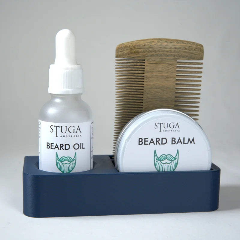 Stuga Australia beard oil and beard balm in white containers with green logo, wooden beard comb, all in navy blue holder