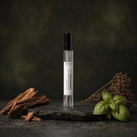 Stuga Cedarwood No. 443 cedarwood perfume, 10ml eau de parfum spray bottle on dark stone with cedarwood shavings, fresh basil leaves and dried botanicals.
