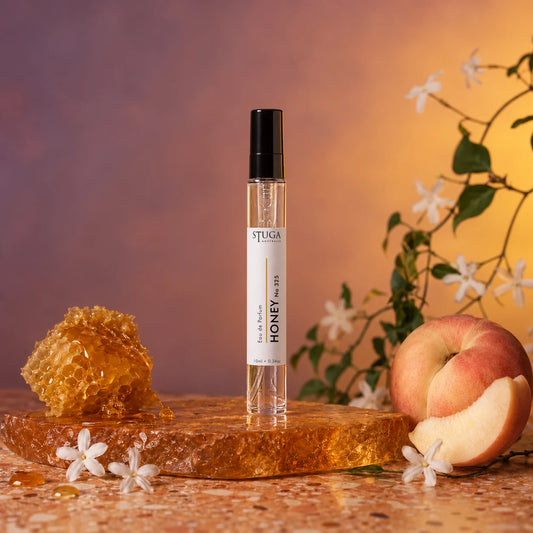 Stuga Honey No. 325 honey perfume, 10ml eau de parfum spray bottle on an amber resin slab with dripping honeycomb, a white peach and wild jasmine blossom.
