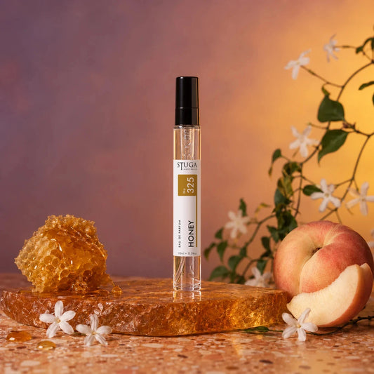 Stuga Honey No. 325 honey perfume, 10ml eau de parfum spray bottle on an amber resin slab with dripping honeycomb, a white peach and wild jasmine blossom.