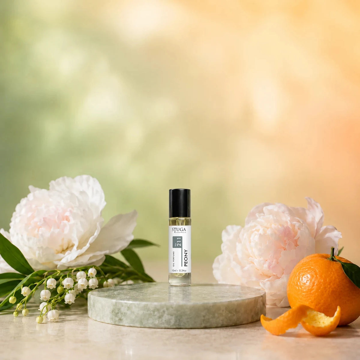 Stuga Peony No. 211 peony oil perfume, 10ml roll-on bottle on a pale green marble disc with white peonies, lily of the valley and a mandarin.