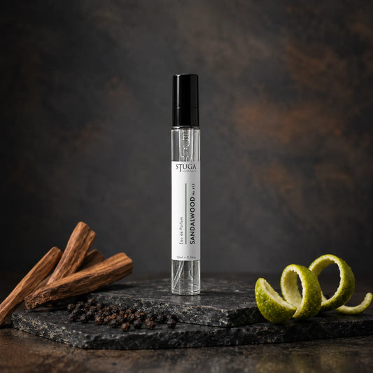 Stuga Sandalwood No. 413 sandalwood perfume, 10ml eau de parfum spray bottle on slate with sandalwood sticks, black peppercorns and a lime peel twist.