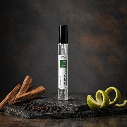 Stuga Sandalwood No. 413 sandalwood perfume, 10ml eau de parfum spray bottle on slate with sandalwood sticks, black peppercorns and a lime peel twist.