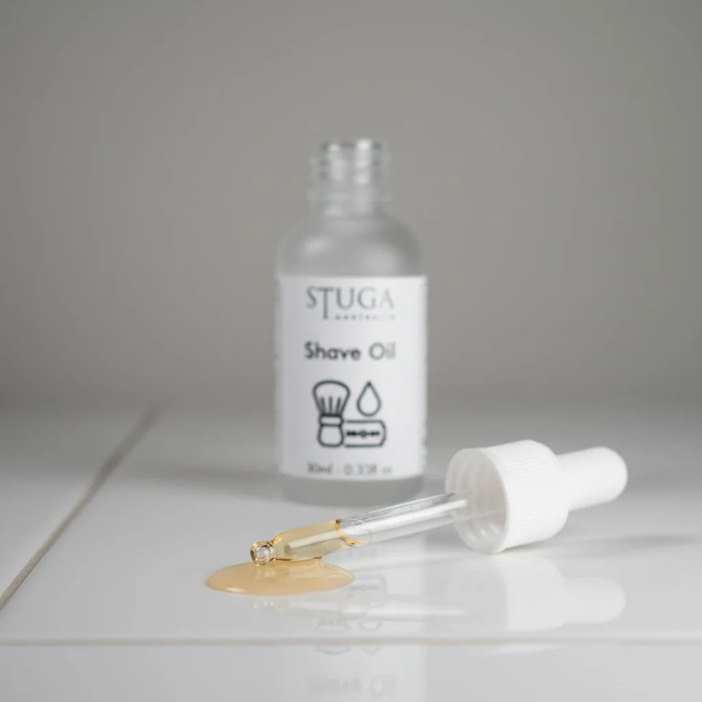 Stuga Australia Shave Oil bottle with a dropper dispensing golden oil onto a white surface.
