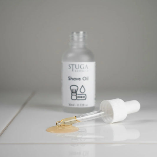 Stuga Australia Shave Oil bottle with a dropper dispensing golden oil onto a white surface.