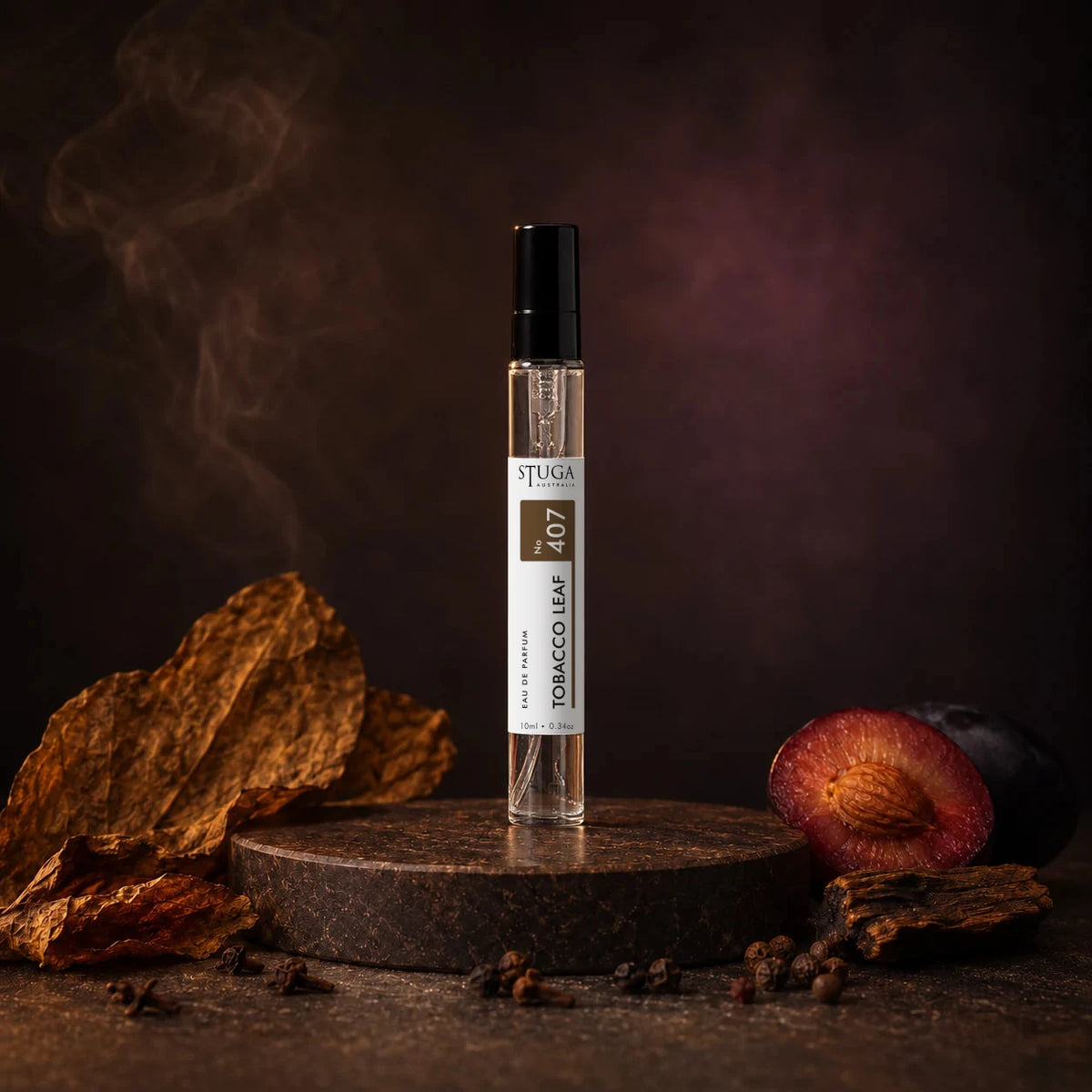 Stuga Tobacco Leaf No. 407 tobacco perfume, 10ml eau de parfum spray bottle on a dark stone plinth with dried tobacco leaves, a spiced plum and drifting smoke.