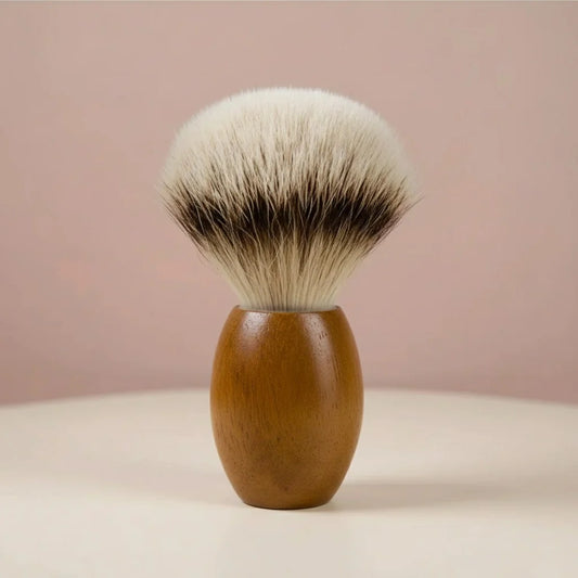 Teak wood handle shaving brush with silver tipped badger bristles, standing upright on a light surface.