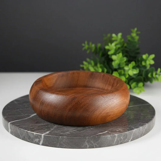 Smooth, round teak wood shaving bowl with a rich brown finish, sitting on a dark marble surface.