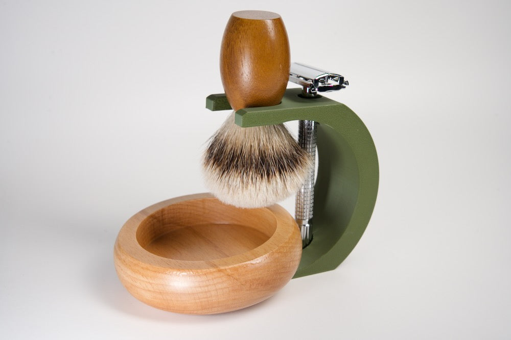 Shaving brush with wooden handle and bowl, green stand, and razor on a white background