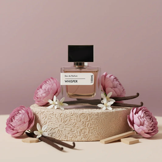 Whisper Eau de Parfum 100ml bottle with black cap, surrounded by pink flowers and vanilla beans on a decorative beige stand.
