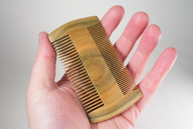 Hand holding a small wooden double-sided comb with fine and wide teeth for hair grooming