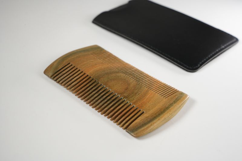 Brown wooden pocket comb with fine and wide teeth alongside a black leather carrying case for grooming