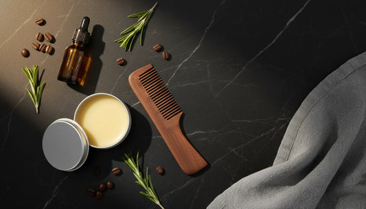 Beard grooming essentials flat lay — beard oil, balm tin and wooden comb on dark marble