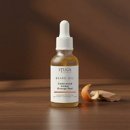 Stuga Beard Oil in Cedarwood, Amber and Orange Peel — amber oil in a glass dropper bottle on warm timber with curled orange peel and cedar offcuts. Made fresh to order with Australian sweet almond, macadamia and apricot kernel oils, handcrafted in the Southern Highlands, NSW Australia.