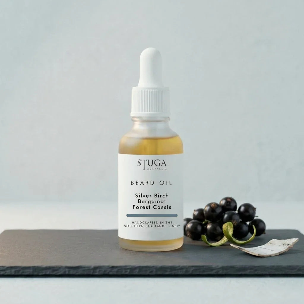 Stuga Beard Oil in Silver Birch, Bergamot and Forest Cassis — amber oil in a glass dropper bottle on a slate slab with fresh blackcurrants and curls of birch bark. Made fresh to order with Australian sweet almond, macadamia and apricot kernel oils, handcrafted in the Southern Highlands, NSW Australia.