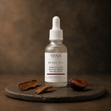 Stuga Beard Oil in Tobacco Leaf, Guaiac Wood and Spiced Plum — frosted glass dropper bottle on a dark stone disc with a curl of cured tobacco leaf, guaiac wood bark and a halved dark plum against a warm brown backdrop. Lightweight beard oil handcrafted in the Southern Highlands, NSW Australia.