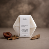 Stuga Beard Wash Block in Tobacco Leaf, Guaiac Wood and Spiced Plum — 100g bar wrapped in plastic-free paper with a halved dark plum, a dried tobacco leaf and a piece of guaiac wood against a warm brown backdrop. Solid beard wash handcrafted in the Southern Highlands, NSW Australia.