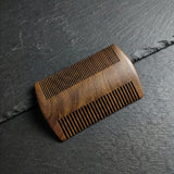 Double-sided black sandalwood beard comb with fine and wide teeth on a dark slate background