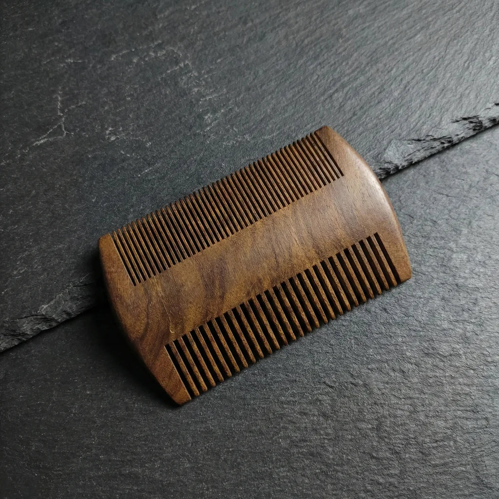 Double-sided black sandalwood beard comb with fine and wide teeth on a dark slate background