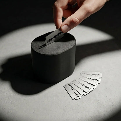Hand dropping a used razor blade into the Stuga Blade Bank disposal case