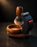 Stuga Complete Shaving Kit shown from the side — badger brush, safety razor, blade sampler, timber bowl and matte black stand on a timber base