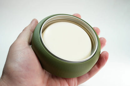 Hand holding a green round travel soap container with a white soap bar inside, ideal for camping and outdoor use