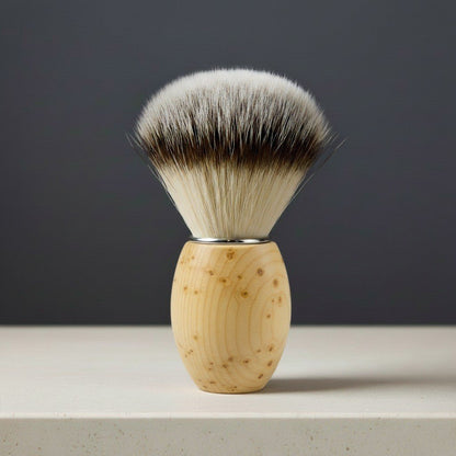 Huon pine wood shaving brush with light-colored synthetic bristles and dark tips, standing upright on a light surface.