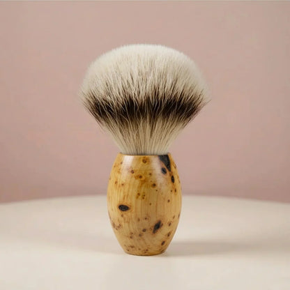 Shaving brush with light brown huon pine wood handle and silver tipped badger bristles, on a light pink background.