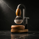 Luxury Magic Shaving Kit — silver tip badger brush with olive wood handle suspended from black arch stand, handturned timber bowl and safety razor on dark marble